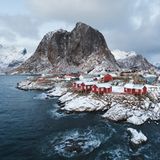 Ein felsiger, mit Schnee bepuderter Küstenabschnitt, mit roten Häusern.