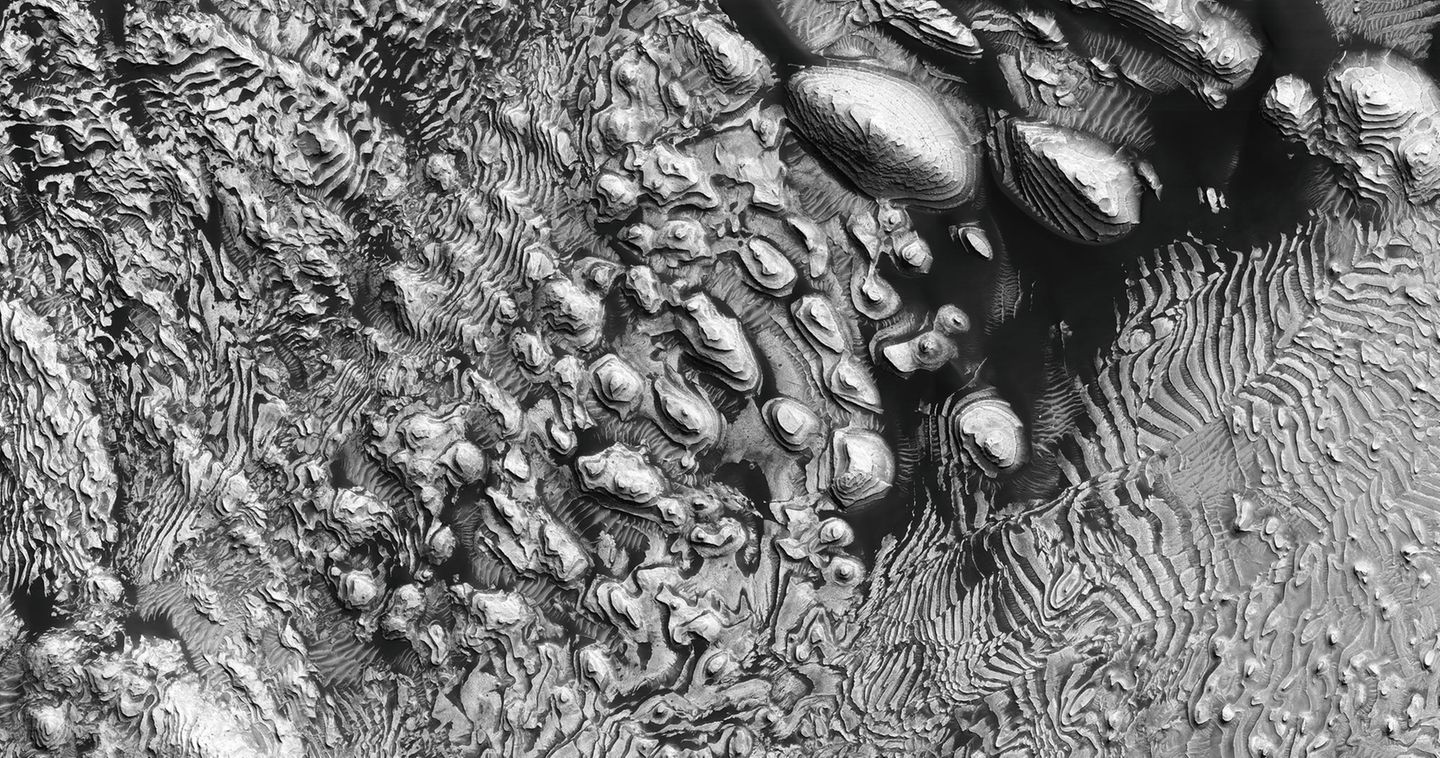 Im Krater pfeift der Wind scharf. Der von ihm mitgetragene Sand lässt die Sedimentschichten erodieren. Da sie ihm unterschiedlich stark Widerstand leisten, bilden sich Treppenstufen heraus. In den windgeschützten Ecken der Stufen sammelt sich dunkler Sand.