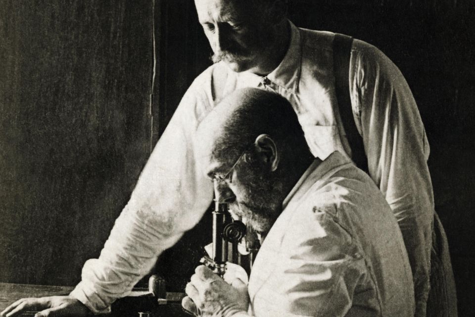 Robert Koch schaut in ein Mikroskop, neben ihm ein Mitarbeiter 0.707