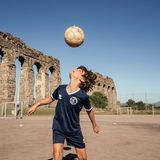 Junge spielt vor den Ruinen eines Aquädukts Fußball