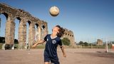 Junge spielt vor den Ruinen eines Aquädukts Fußball