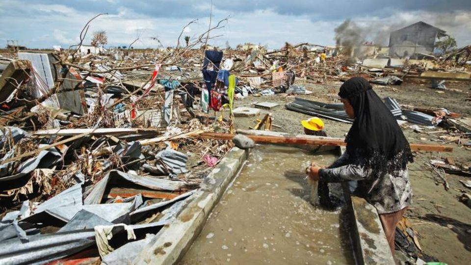 Eine Frau in Banda Aceh (Indonesien) sucht in einem Trümmerhaufen nach Habseligkeiten