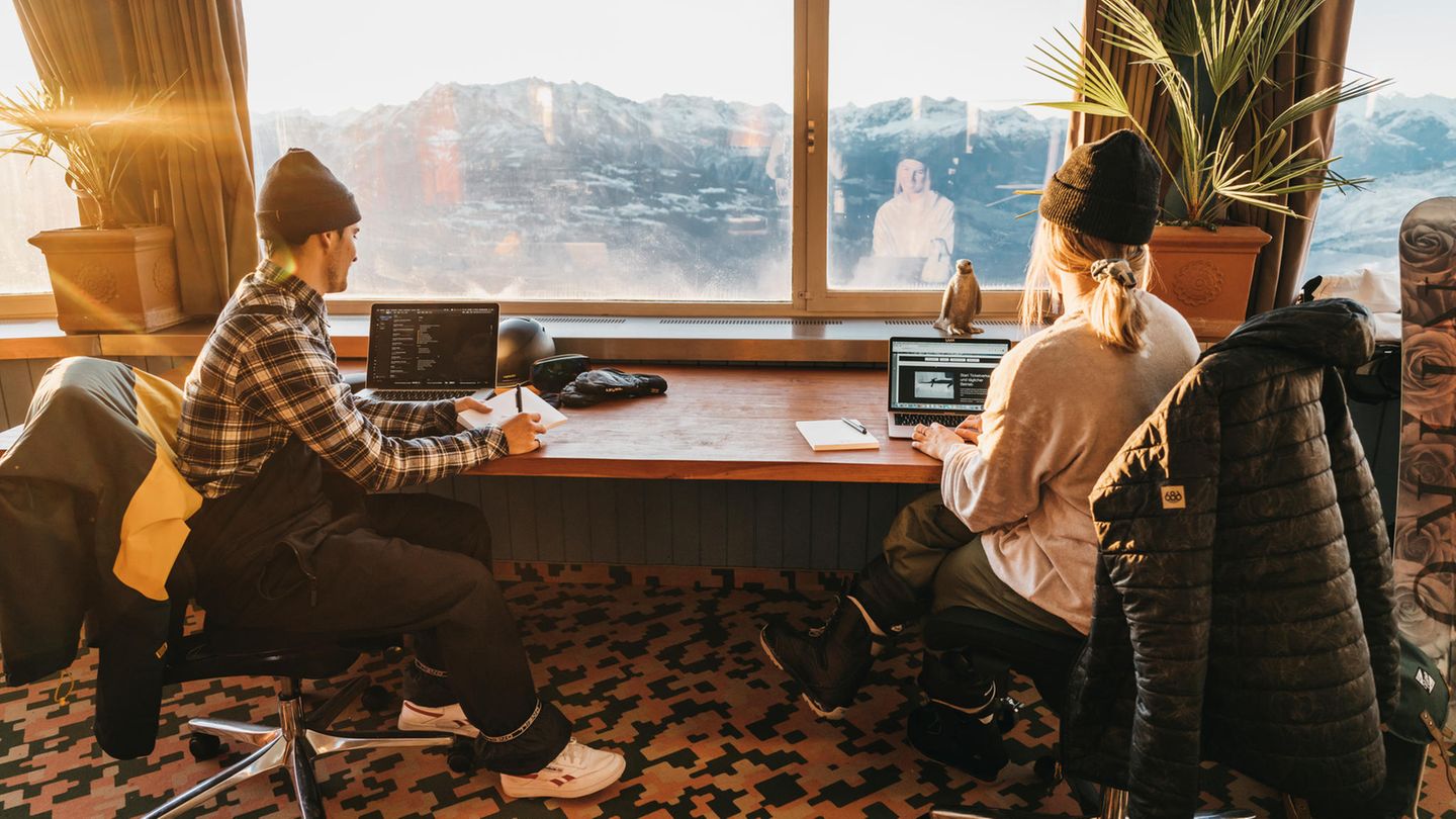 Zwei junge Menschen sitzen vor einem Fenster und arbeiten am Laptop