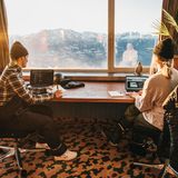 Zwei junge Menschen sitzen vor einem Fenster und arbeiten am Laptop