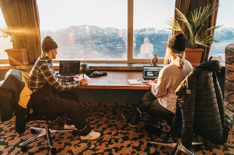 Zwei junge Menschen sitzen vor einem Fenster und arbeiten am Laptop