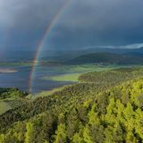 Im Hintergrund ein See, vorne Wald und ein Regenbogen