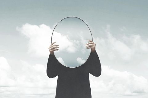 Person hält Spiegel mit Wolken vor sich