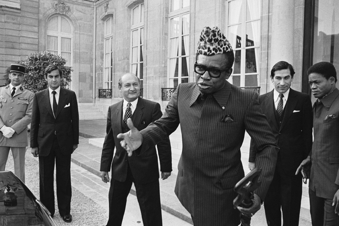 Zaire: Zum Einkaufen mit Überschall Mobutu mit Leopardenfellmütze vor einem Palast, hinter ihm mehrere Männer