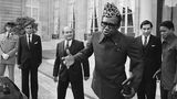 Mobutu mit Leopardenfellmütze vor einem Palast, hinter ihm mehrere Männer