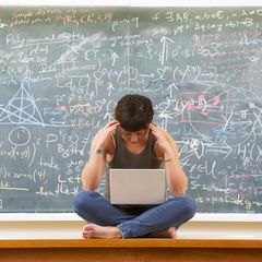 Schülerin sitzt vor großer Tafel mit Mathematikformeln und denkt