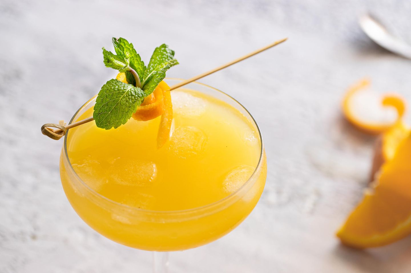 Ein, mit orange leuchtendem Aqua de Valencia, gefülltes glas. Garniert mit Orangenschale und Minzblatt, von oben fotografiert.