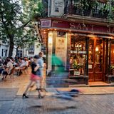 Eine erleuchtete Bar, an der Menschen vorbei flanieren.