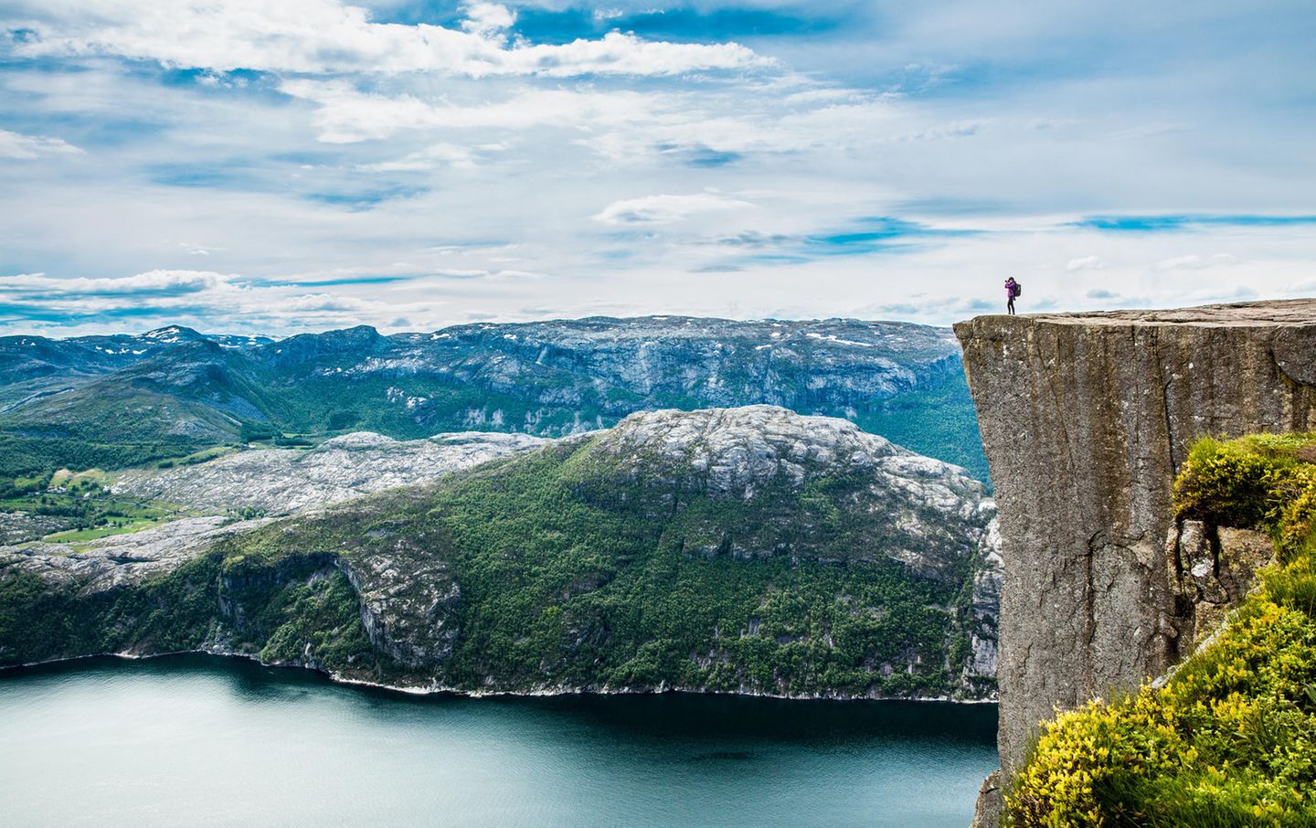 Ein Mensch steht auf der Viereckigen Felskante und blickt über die weite Landschaft.
