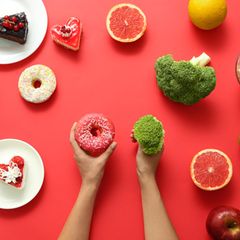 links liegen ungesunde Lebensmittel, rechts gesunde, je eins davon wird in der Hand gehalten