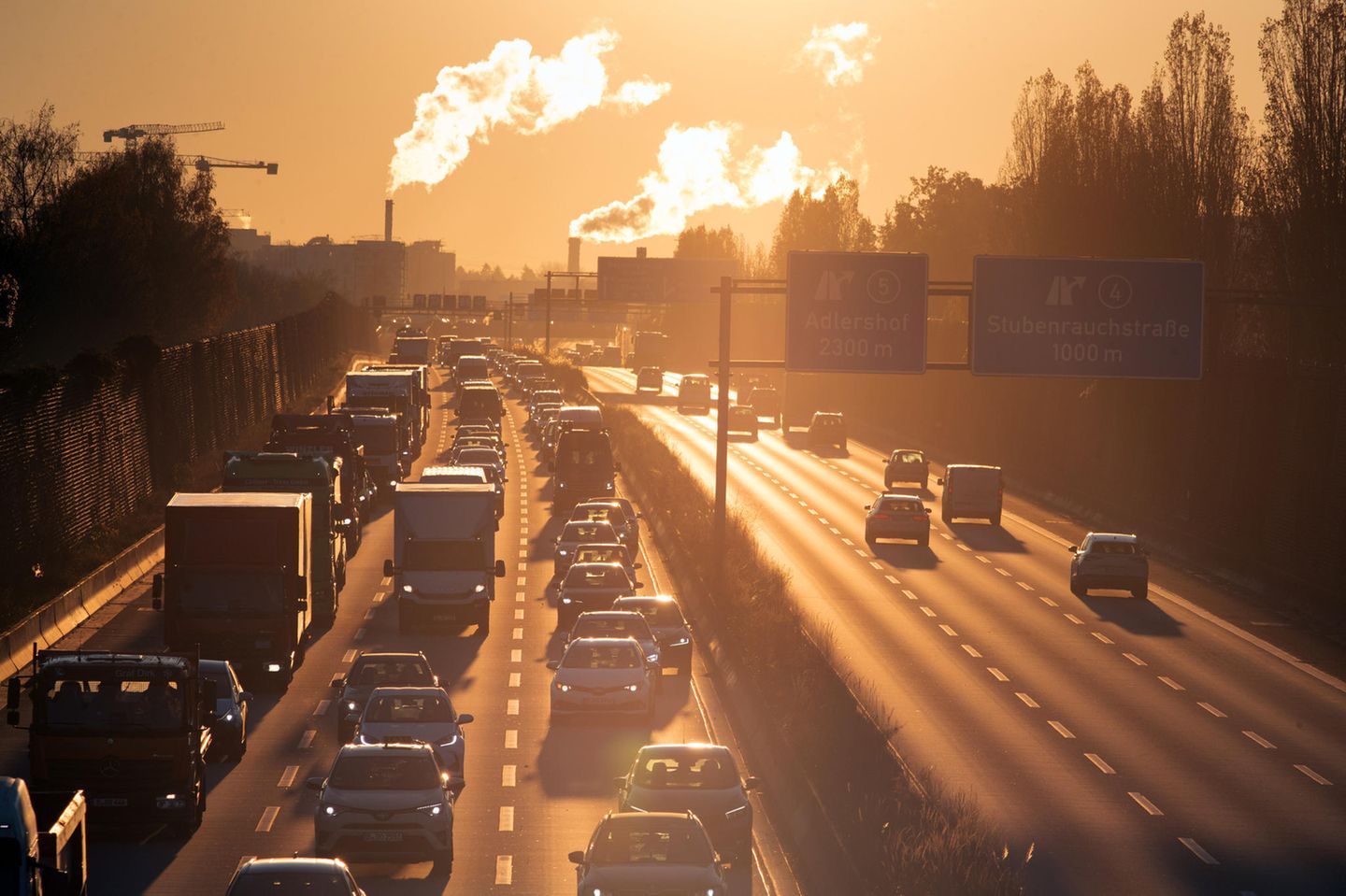 Stau auf der Autobahn bei Sonnenaufgang. Im Hintergrund Emissionen aus Industrieschloten.