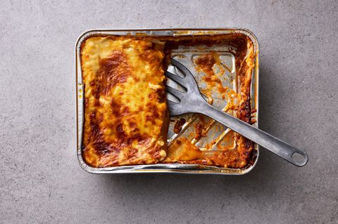 Halb aufgegessene Lasagne in Aluschale mit Pfannenwender