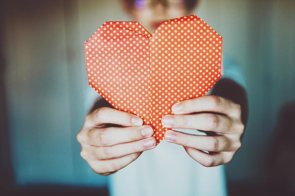 Ein KInd hält ein rotes Origami Herz hoch 1.5004