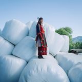 Frau in griechischer Tracht steht auf weiß verpackten Heuballen