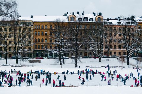 Eisfläche mit Schlittschuhfahrern, dahinter alte Häuser