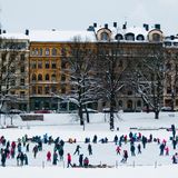 Eisfläche mit Schlittschuhfahrern, dahinter alte Häuser