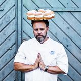 Mann mit geschlossenen Augen balanciert Tablett mit Gebäck auf dem Kopf