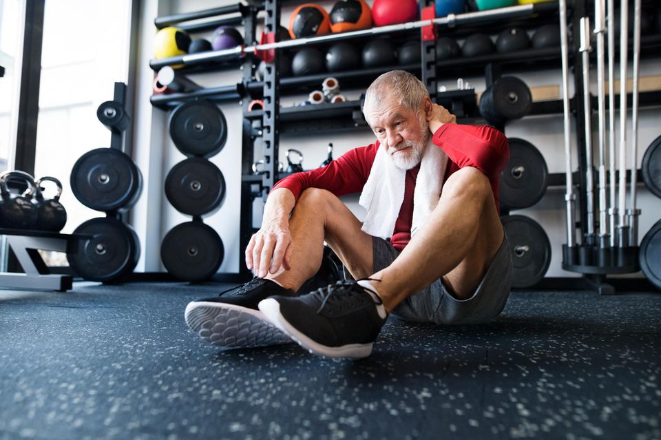 Ein älterer Mann trainiert mit Muskelkater in einem Fitnessstudio 1.5004