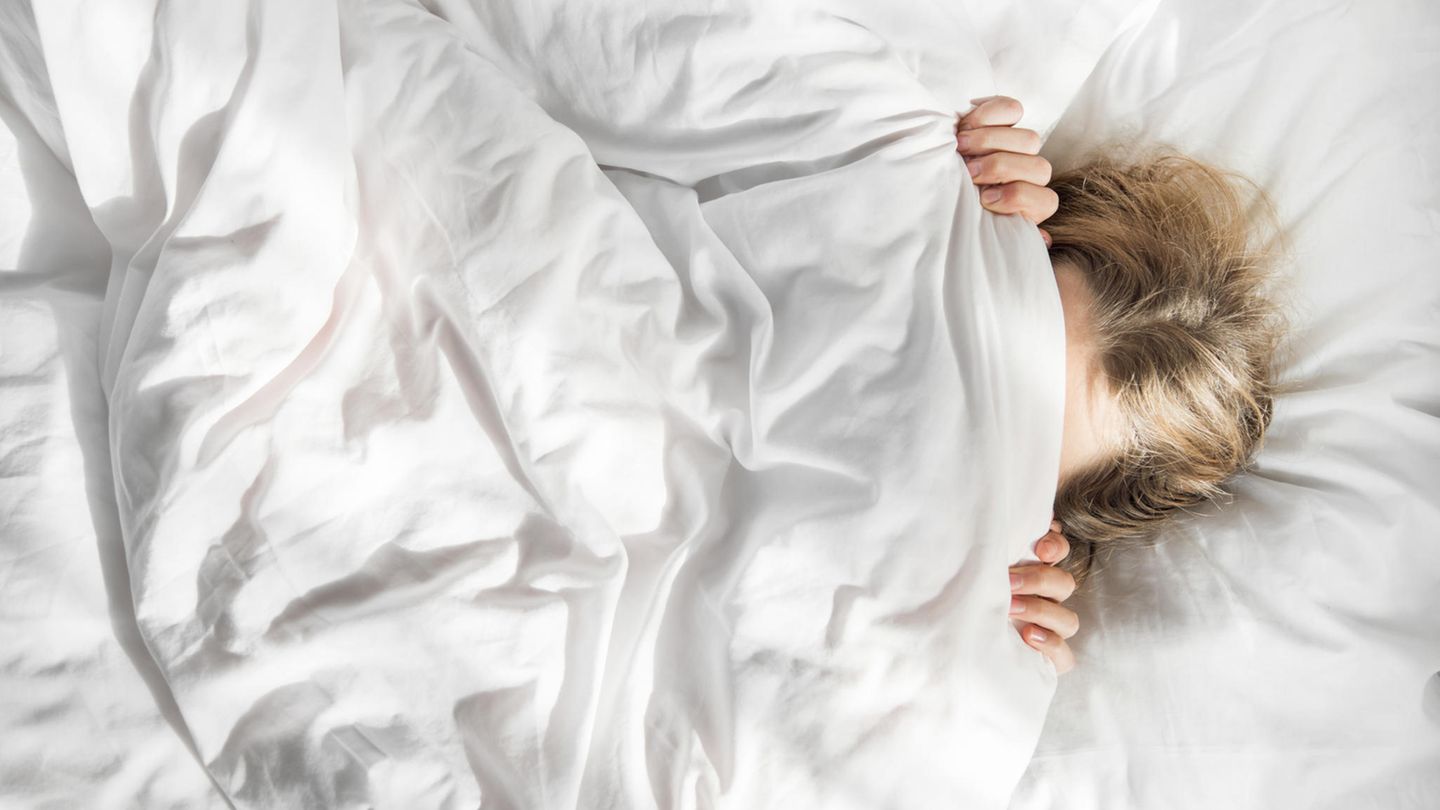 Im Morgenlicht zieht sich eine Frau im Bett die Decke übers Gesicht Im Morgenlicht zieht sich eine Frau im Bett die Decke übers Gesicht