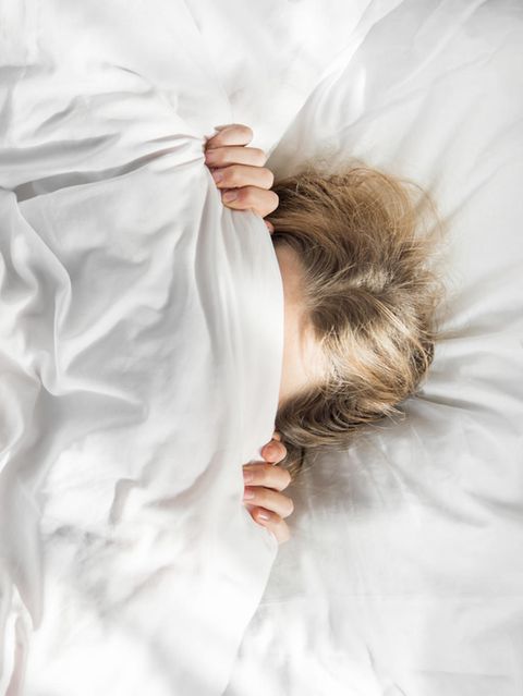 Im Morgenlicht zieht sich eine Frau im Bett die Decke übers Gesicht