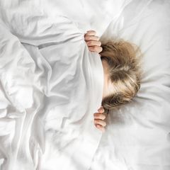 Im Morgenlicht zieht sich eine Frau im Bett die Decke übers Gesicht