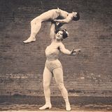 Eine Frau in ballettähnlicher Kleidung trägt einen Mann auf ihrem gestreckten rechten Arm