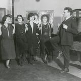 Ein Mann im schwarzen Anzug macht einer Gruppe schwarz gekleideter Frauen Bewegungen vor