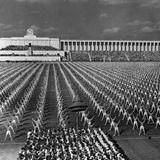 Turner in unzähligen Reihen machen exakt die gleichen Übungen, im Hintergrund gewaltige Gebäude