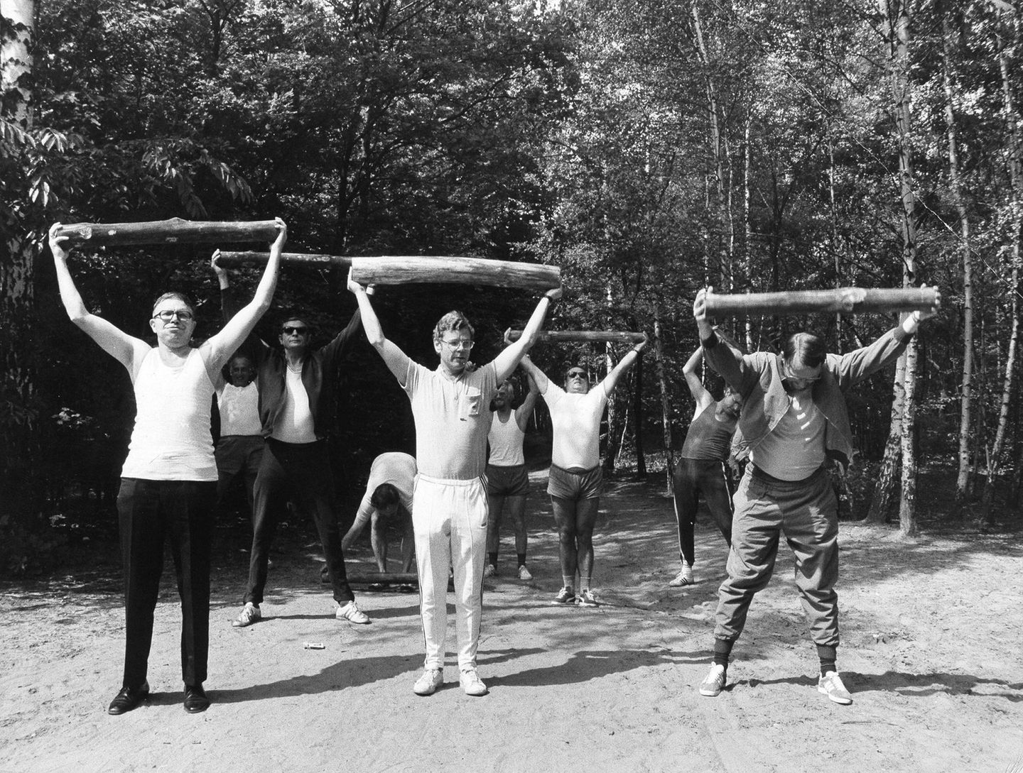 Sport der Undisziplinierten Mehrer Männer strecken auf einem Waldweg kurze Holzstämme waagerecht über ihre Köpfe