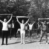 Mehrer Männer strecken auf einem Waldweg kurze Holzstämme waagerecht über ihre Köpfe