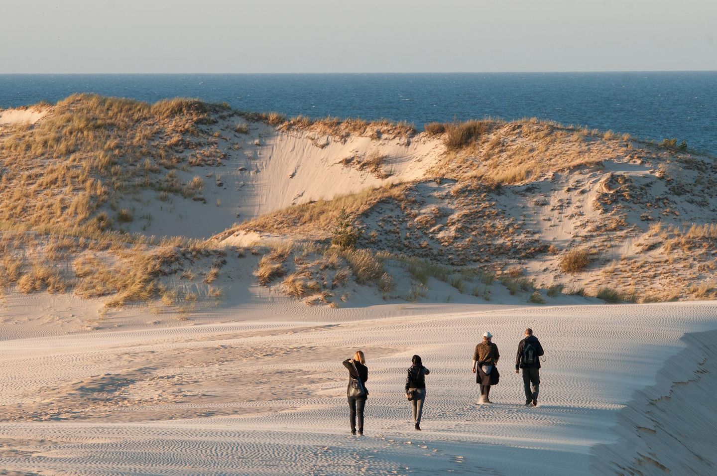 Menschen wanderen auf einer Düne in Richtung des Meeres