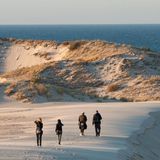 Menschen wanderen auf einer Düne in Richtung des Meeres