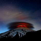 Die Lava des Vulkans Villarrica beleuchtet eine kreisförmige, zweischichtige Wolke die, die Spitze  Vulkans umhüllt.