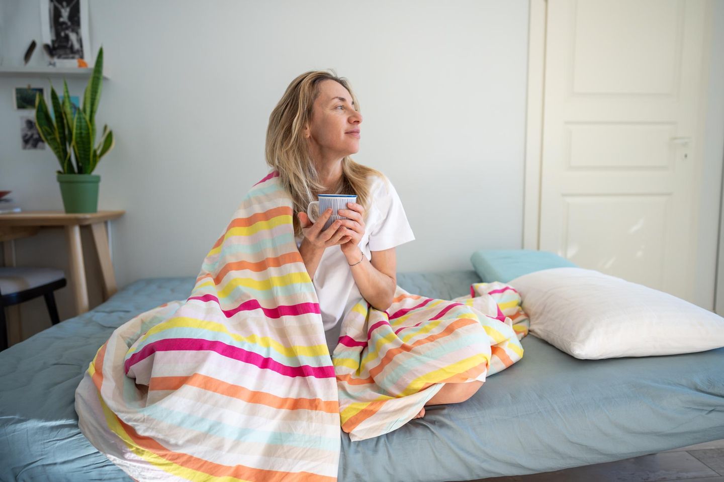 Eine in eine Bettdecke gehüllte Frau im Bett mit einer Tasse Kaffee