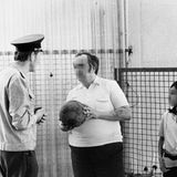 Mann hält Fußball in der Hand und steht neben einem Beamten