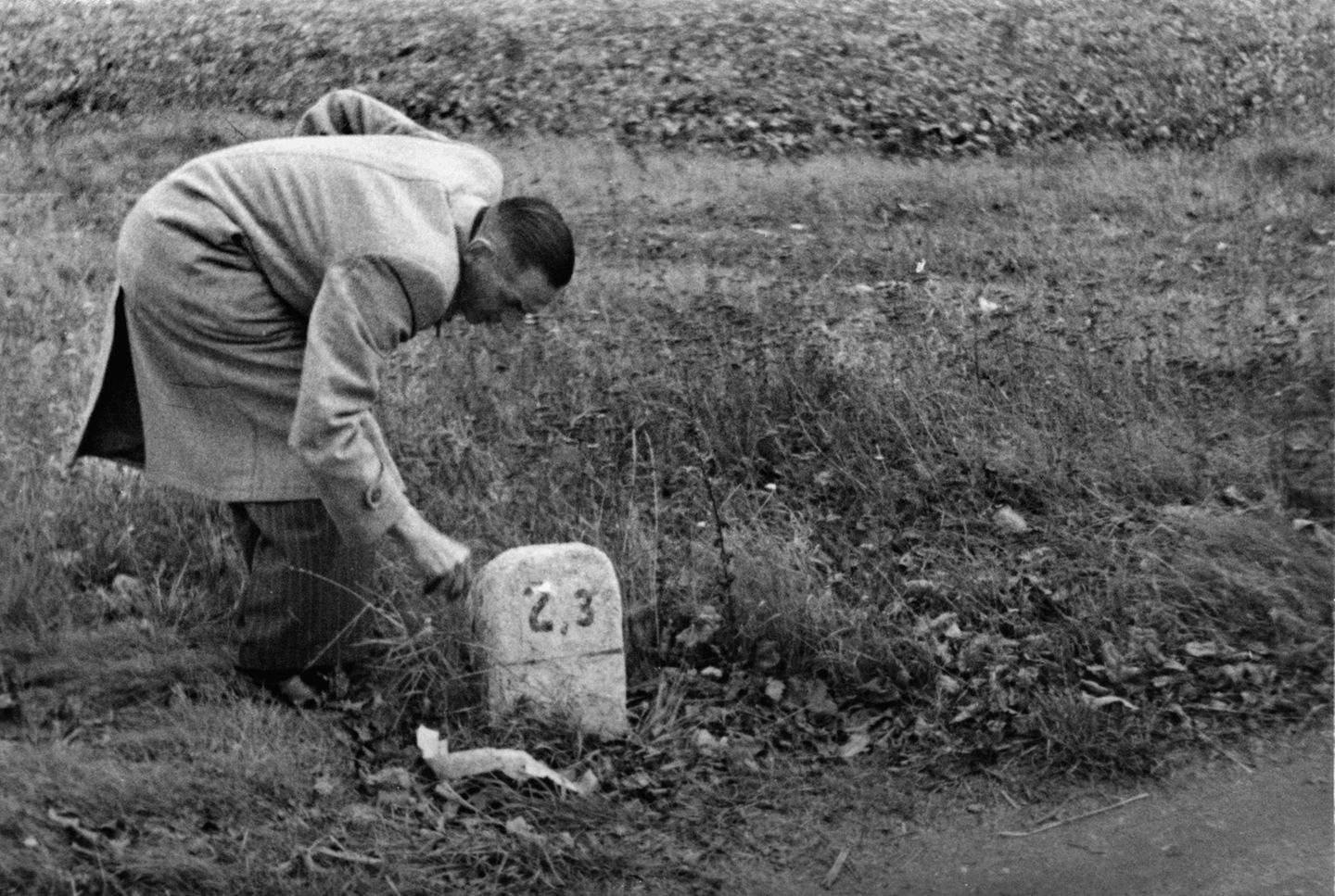 Mann streckt Hand nach einem toten Briefkasten hinter einem Kilometerstein aus