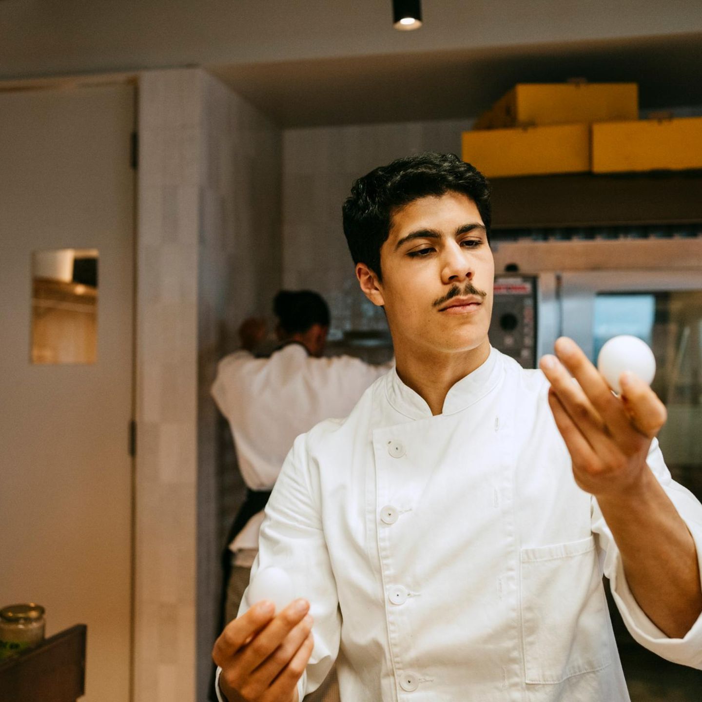 Ein Mann mit Schnauzbart begutachtet ein Hühnerei in seiner linken Hand