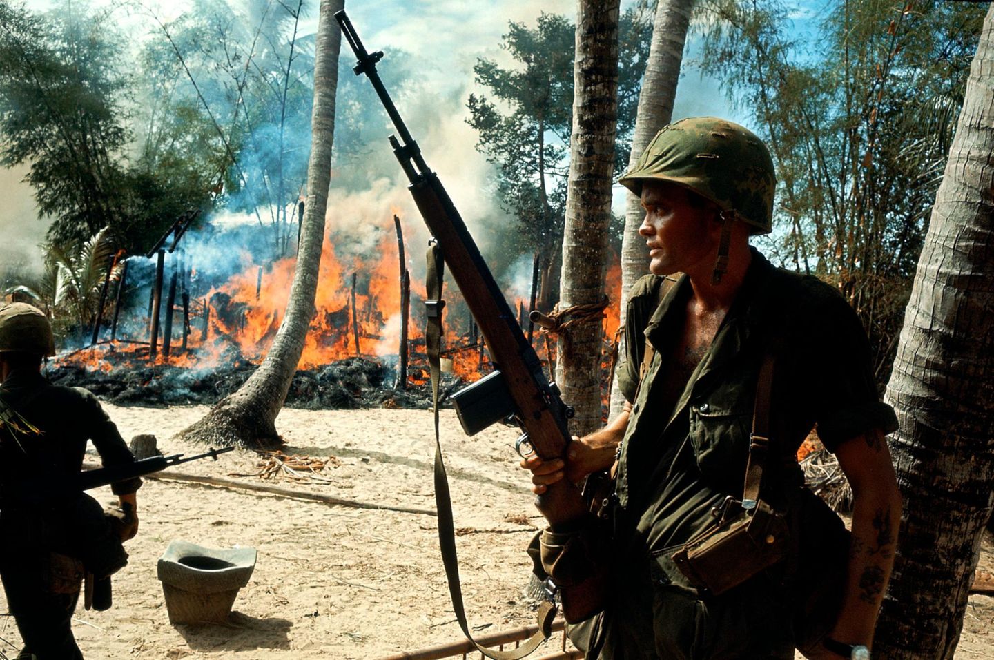 Soldat im Vietnamkrieg steht vor brennendem Dorf