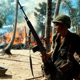Soldat im Vietnamkrieg steht vor brennendem Dorf