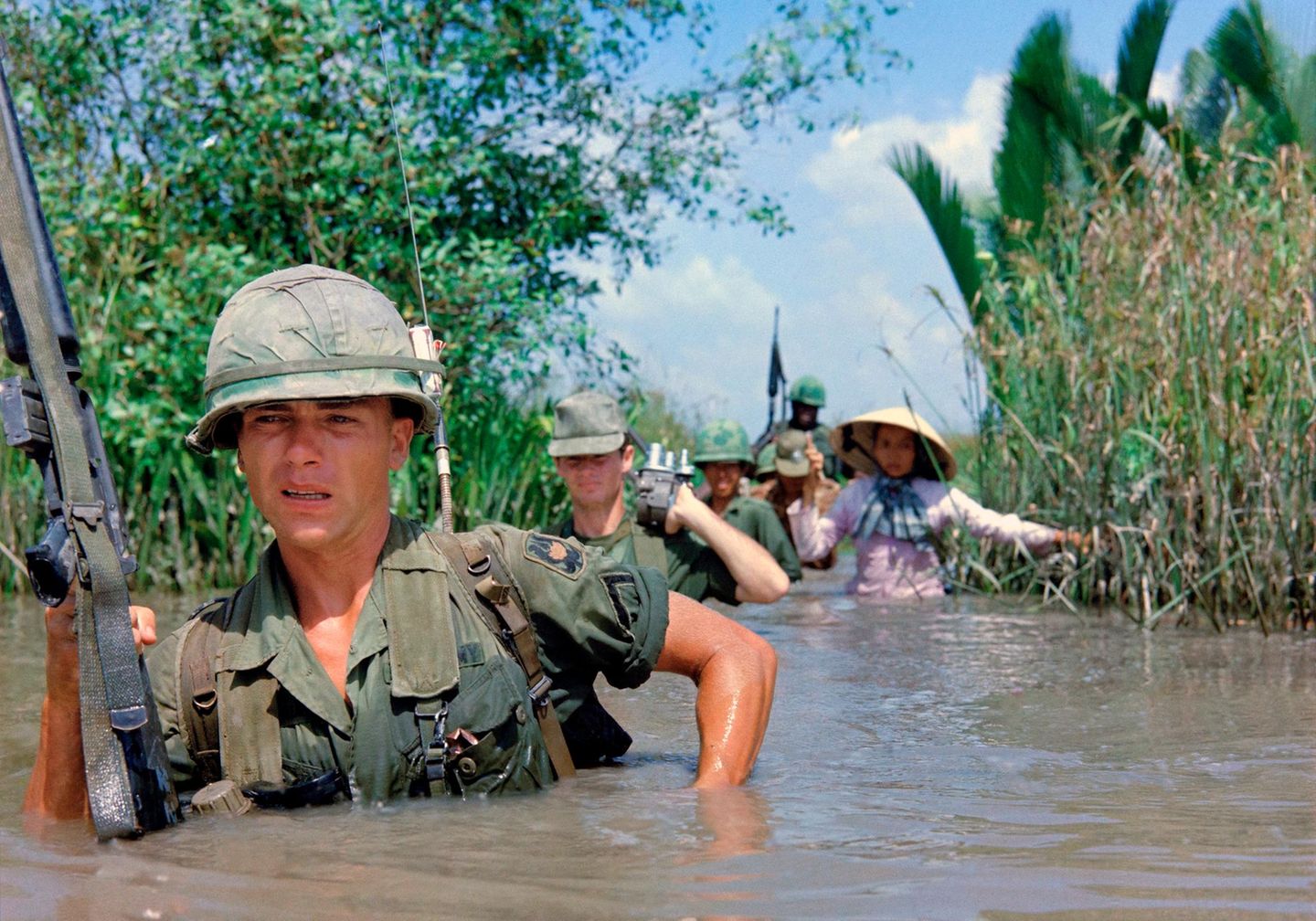 Mühsame Patrouille durch tropisches Gelände US-Soldat durchquert einen tiefen Bewässerungskanal zusammen mit Mitgliedern der 5th ARVN Ranger Group