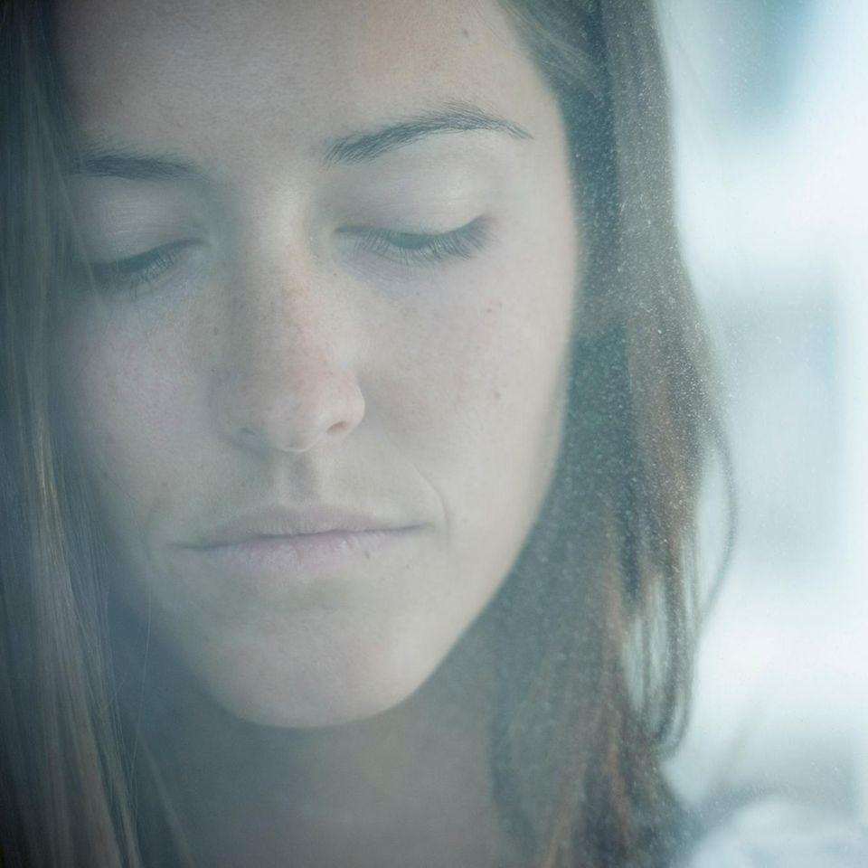 Eine Frau schaut traurig durch eine beschlagene Fensterscheibe