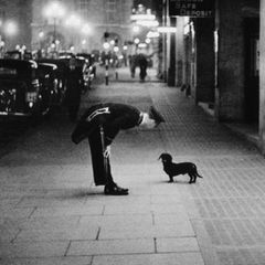 Commissionaire's Dog  A hotel commissionaire talking to a small dachshund dog in Piccadilly Circus, London. Original  Publication: Picture Post - 2 - In The Heart of the Empire - pub. 1938 