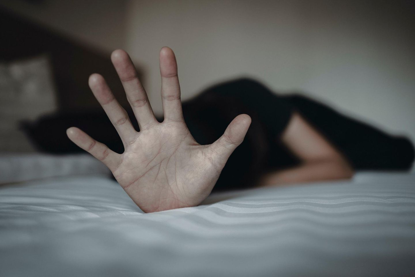 Frau auf Bett liegend, streckt die Hand abwehrend von sich