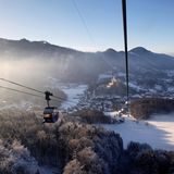 Blick aus einer Gondel der Kampenwandbahn auf verschneite Wälder und Schloss Hohenaschau in der Abensonne