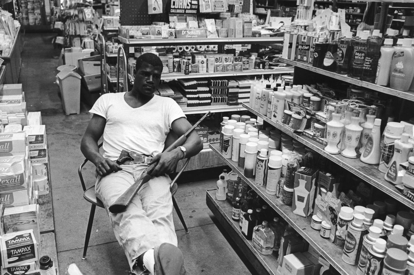 Mann sitzt mit Gewehr auf Stuhl in Geschäft