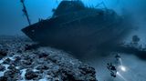 Im Roten Meer, Ägypten, gelang diese Aufnahme von einem gesunkenen Schiffswrack in knapp über 100 Meter Tiefe. Es liegt so auf zwei Riffen, dass die Taucher darunter durchtauchen können.